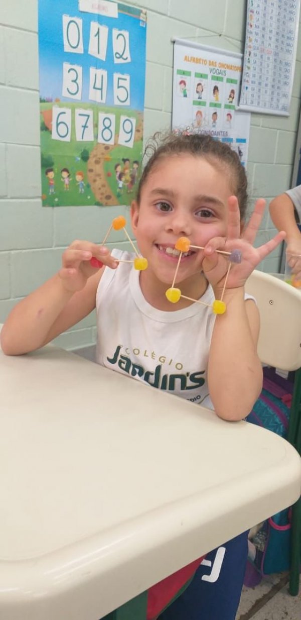 A professora Camilla propôs aos alunos do 1º ano uma  atividade lúdica e prática para a fixação dessa temática. Utilizando recursos como palitos e jujubas, cada estudante produziu sua próprio figura geométrica.